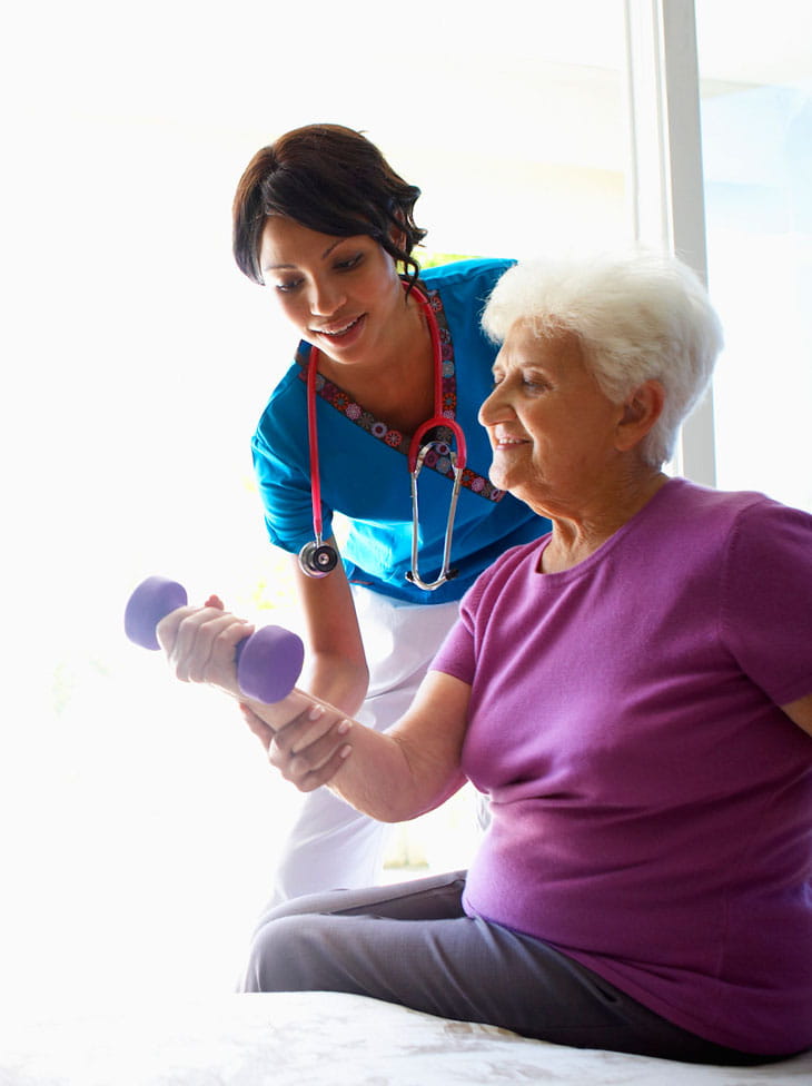 A woman lifts a small weight with help from a care professional.